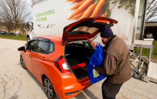 Photo of a man loading bags of food into a car at a VeggieVanGo event.