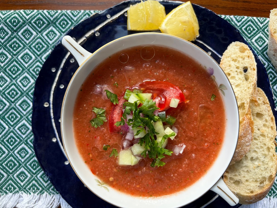 Photo of Gazpacho Andaluz in a bowl with bread slices and lemon wedges.