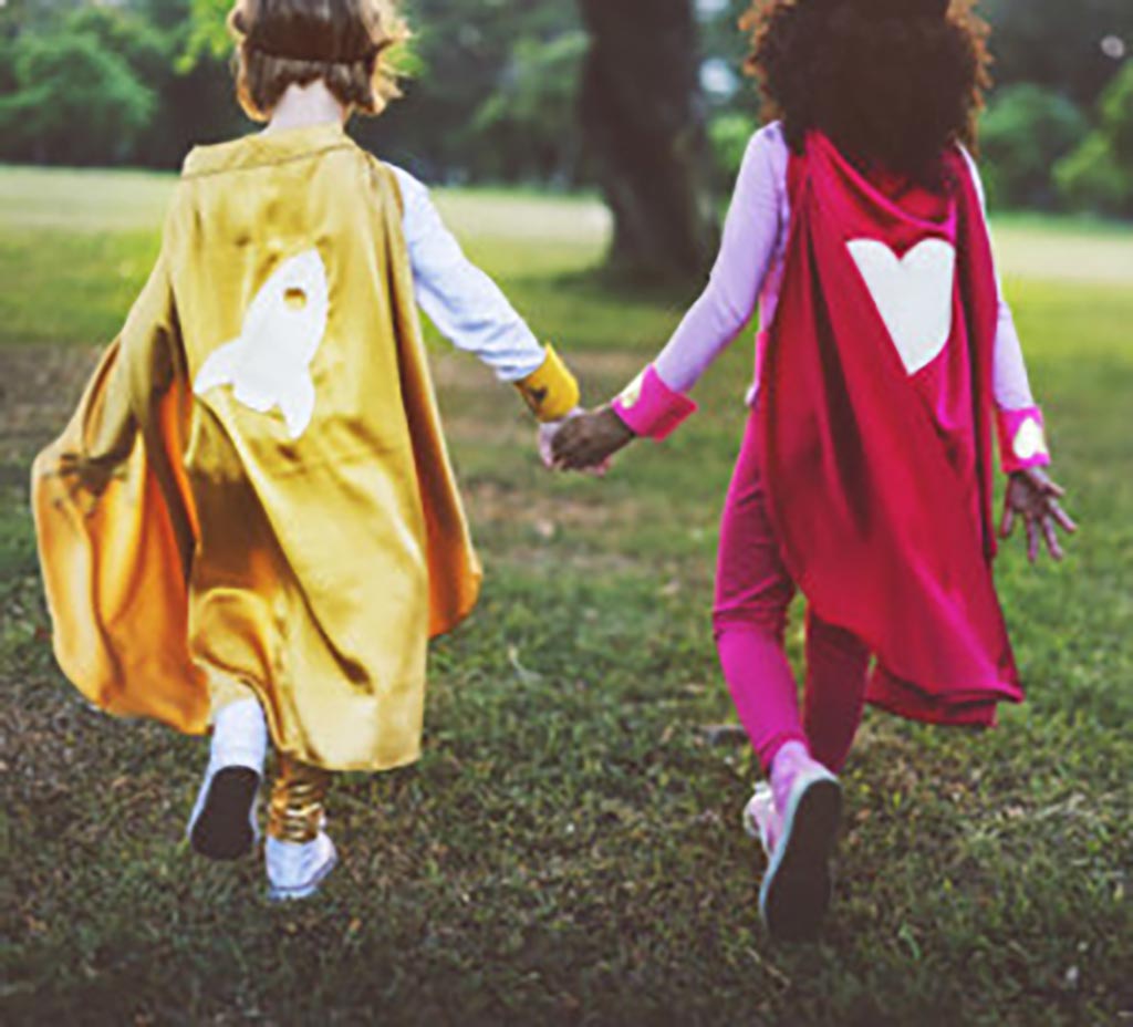 20240227_kidsHandsLg Two children wearing capes walk away from the camera holding hands.