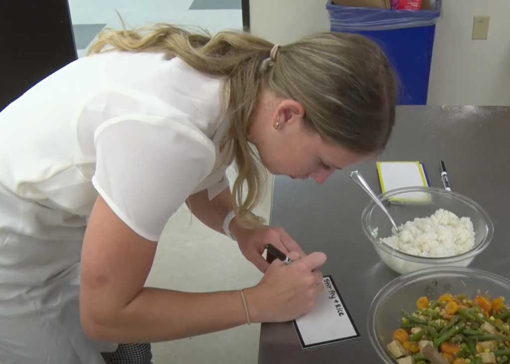 Photo of a nutritionist writing out a recipe card with ingredients in front of her. 