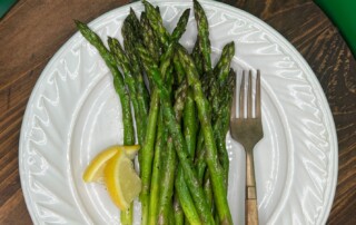 Photo of Sauteed Asparagus spears on white dish with wedge of lemon and fork