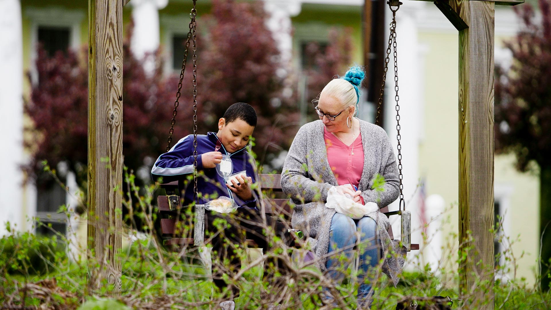 Image of a young boy and a woman sitting on a bench enjoying some food.