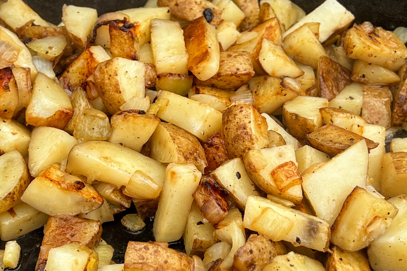 Photo of cubed potatoes and diced onion onions sautéing in cast iron skillet