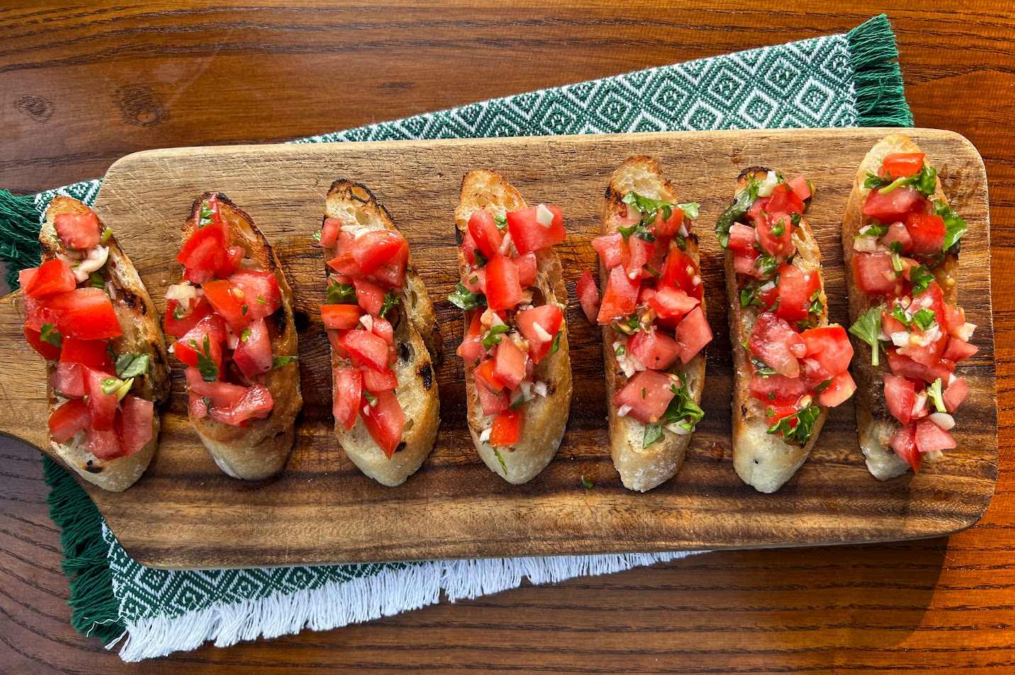 5 pieces of Tomato Bruschetta on cutting board that is placed on top of green napkin